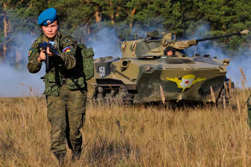 A cadet advances as armored support rumbles behind.